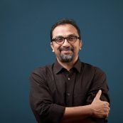 Portrait of a smiling man of Indian ethnicity against a blue wall background.